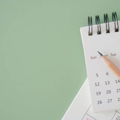 top view of white calendar and sharpen brown pencil on green background, schedule, timeline, planning concept